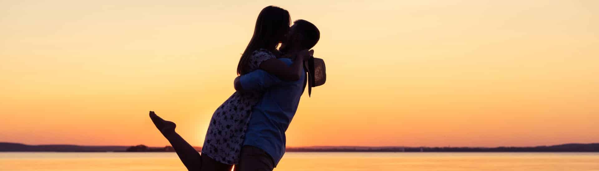 A man and woman embracing at sunset by a body of water