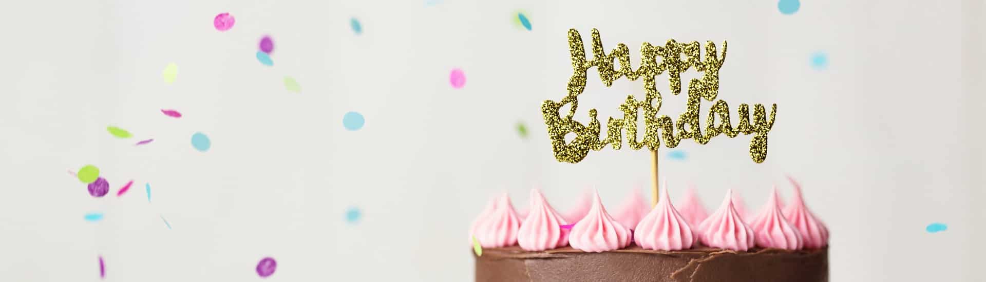 Cake with chocolate and pink frosting with gold happy birthday sign and confetti in the air