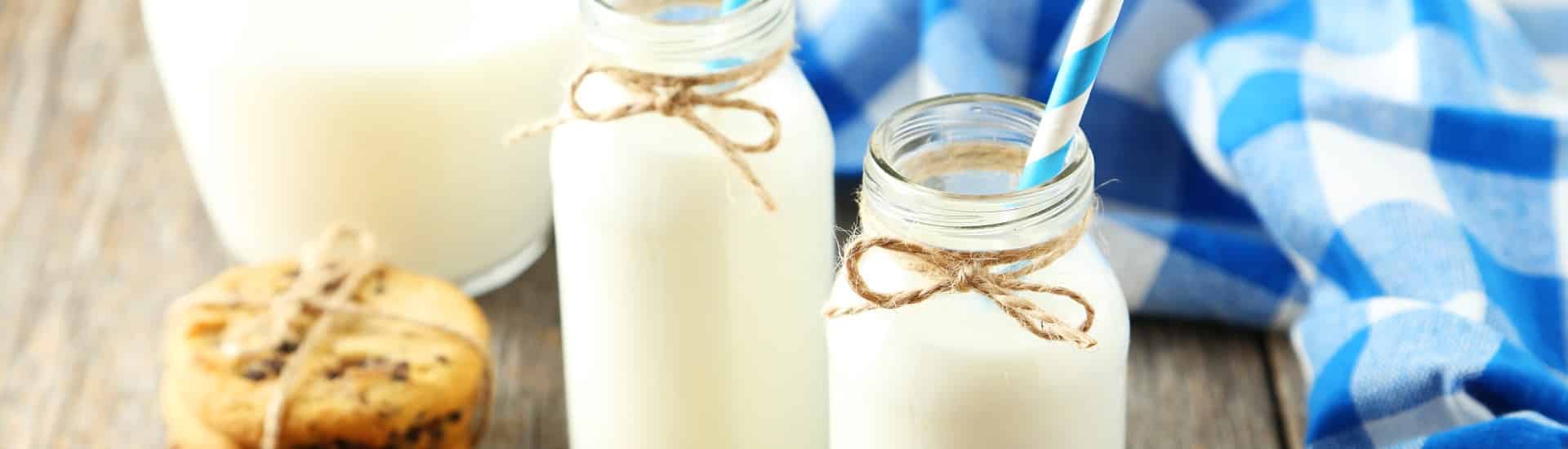 Two glass jars of milk with striped straws next to a stack of cookies