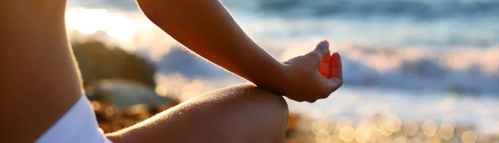 Woman in white bathing suit meditating on the beach with bright sunlight