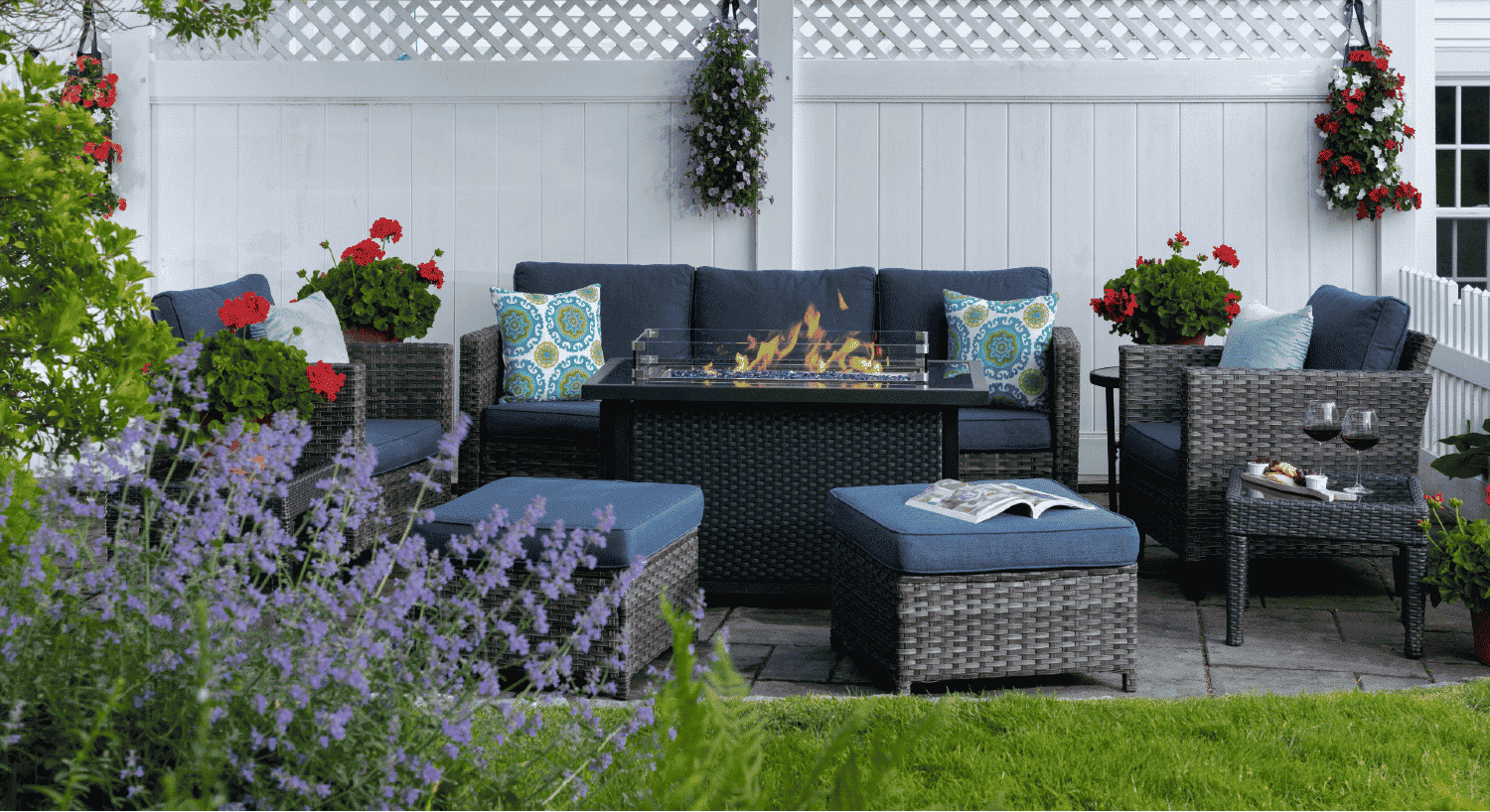 Outdoor fire pit area with wicker furniture with blue cushions by white privacy fence