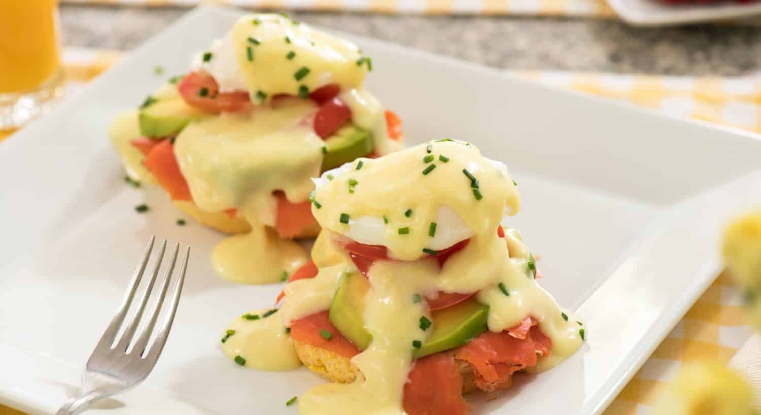 Square white plate with two breakfast egg muffins with tomato, avocado and hollandaise sauce
