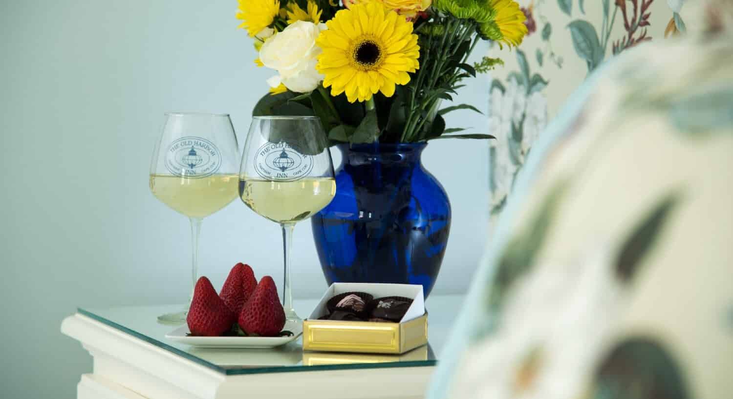 Two chocolates, strawberries, two glasses of wine and flowers in a blue vase on a glasstop table
