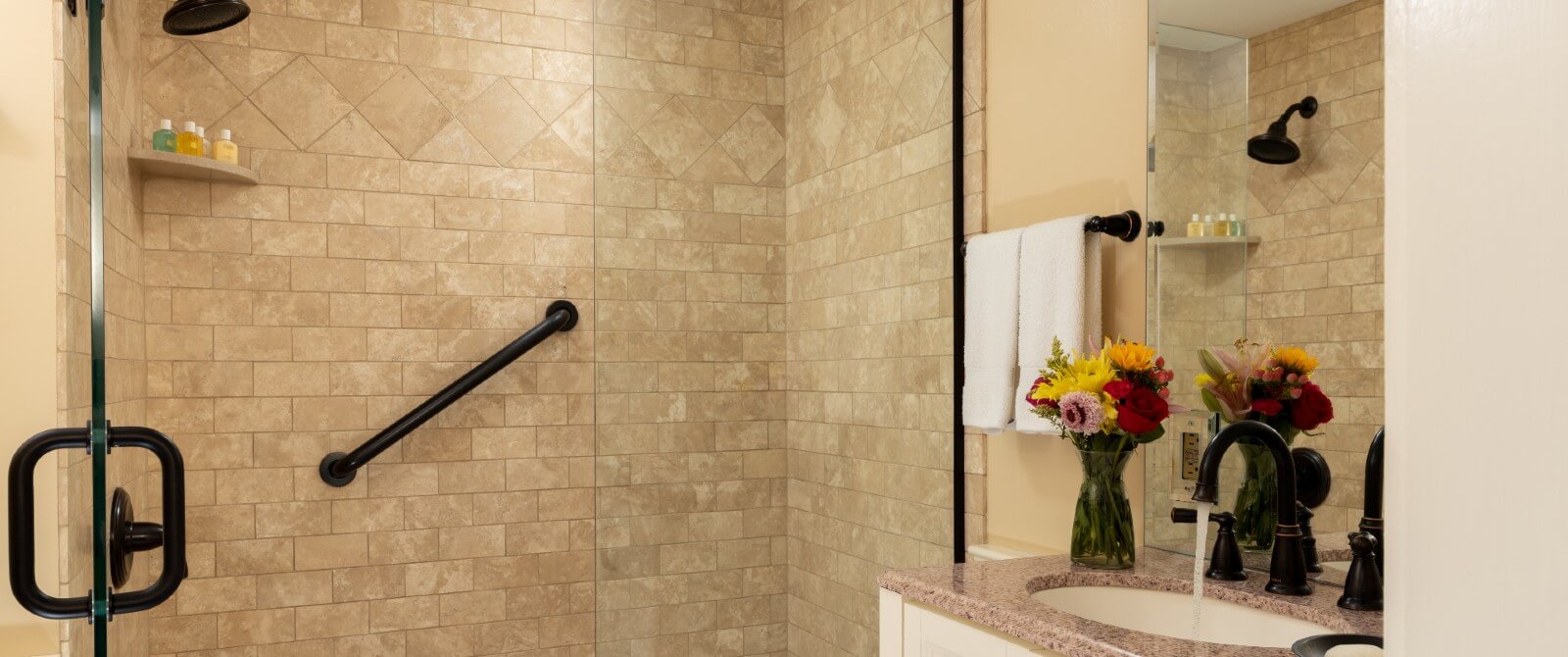 Bathroom with large shower with glass doors and vanity with vase of flowers