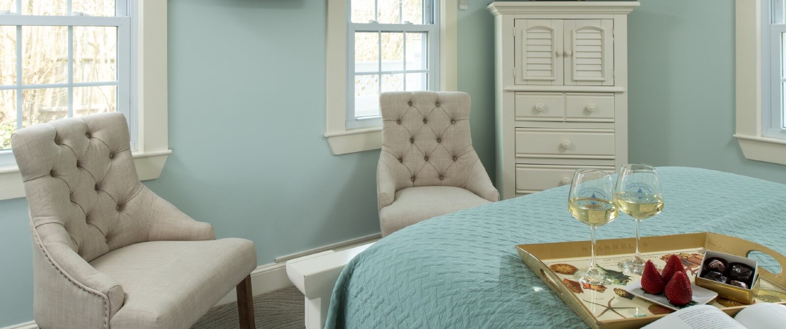 Bedroom with two sitting chairs, dresser and bed with tray of wine glasses, chocolates and strawberries