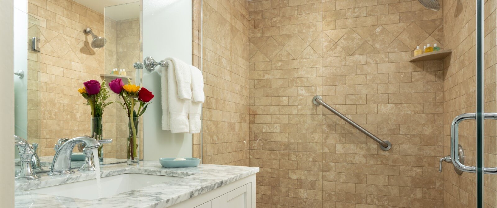 Bathroom with large tiled shower and vanity with granite countertop and vase of flowers