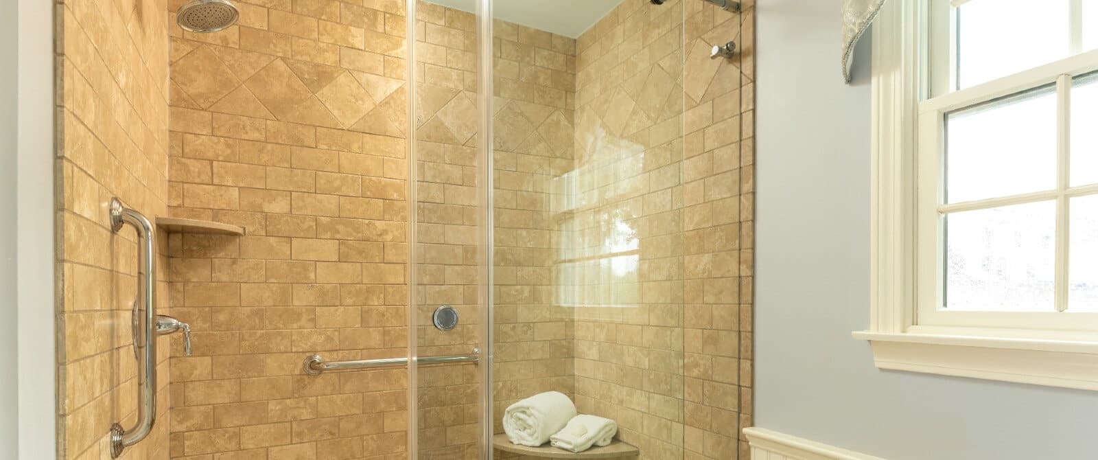 Large tiled shower with glass doors next to a bright window