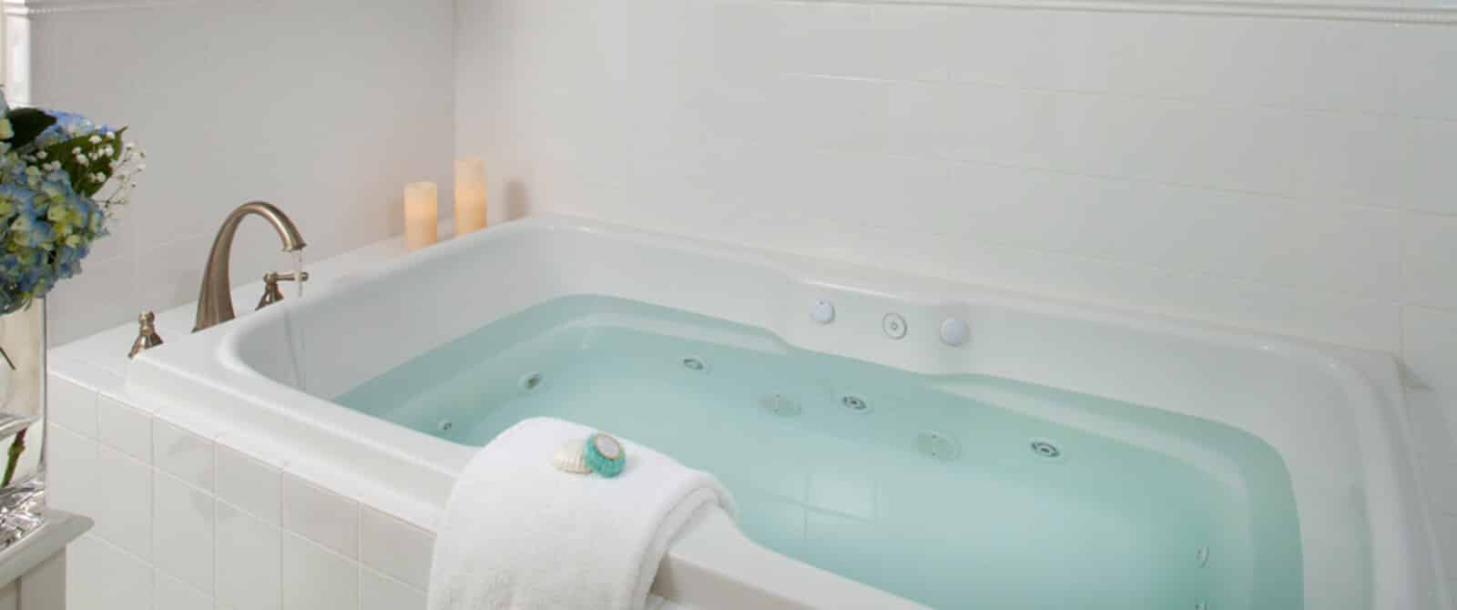 Large, white jet tub filled with water with candles and a folded white towel