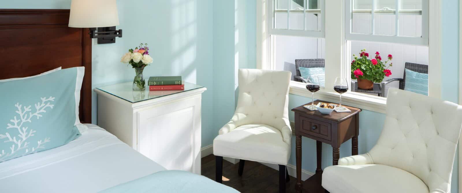 Bedroom with pale blue hues, white sitting chairs and window overlooking private patio