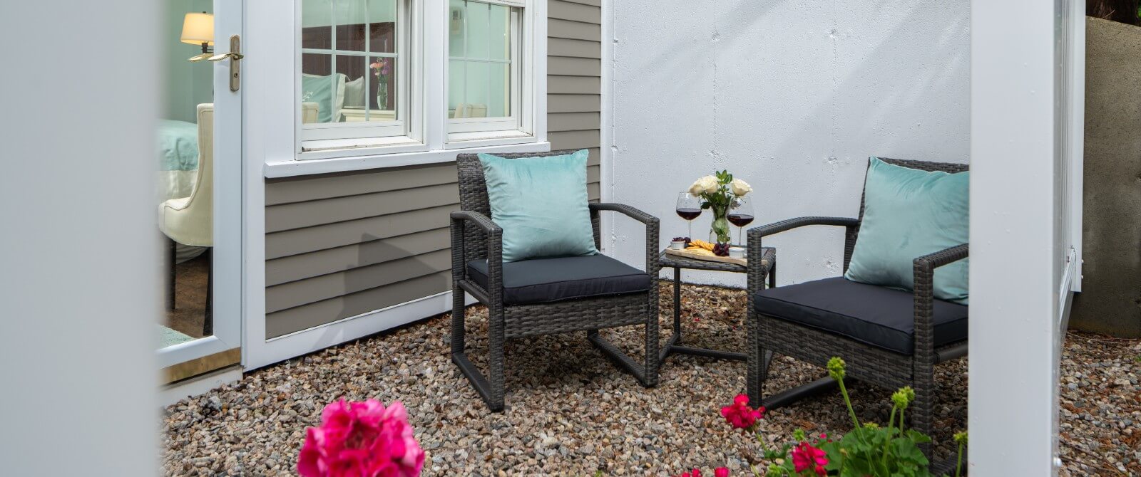 Outdoor patio outside of a bedroom with two chairs and table with wine glasses and vase of flowers