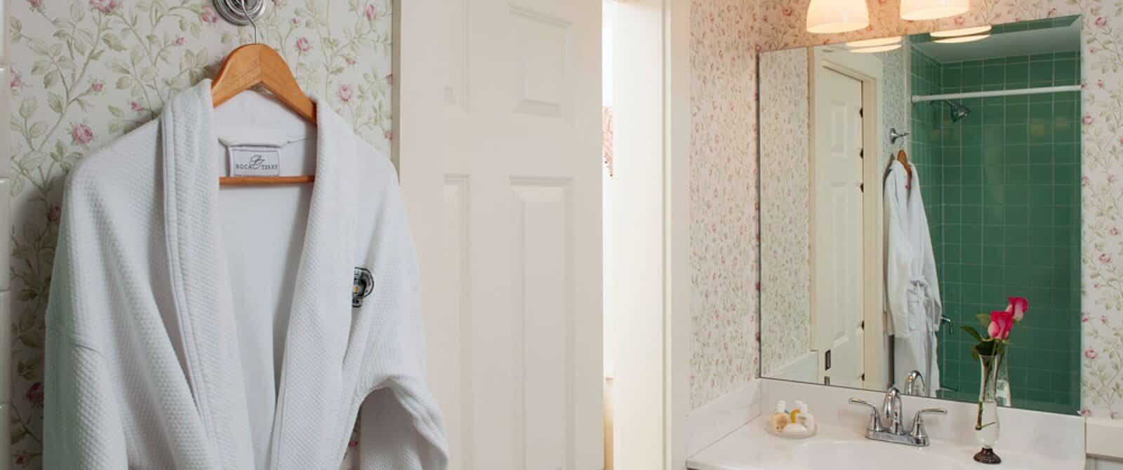 White bathrobe hanging by open doorway to bathroom with single sink and green tiled shower