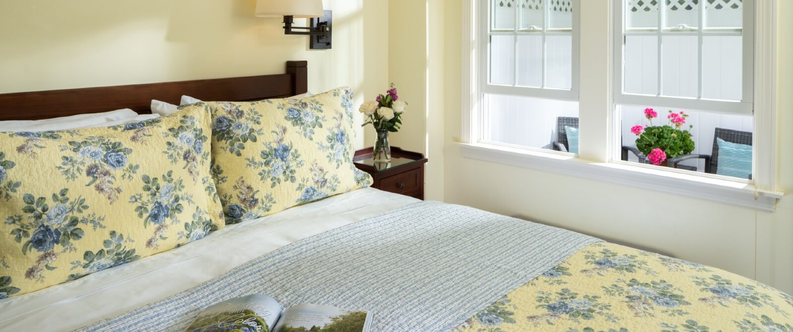 Bright bedroom with bed in floral quilt and window overlooking to private patio