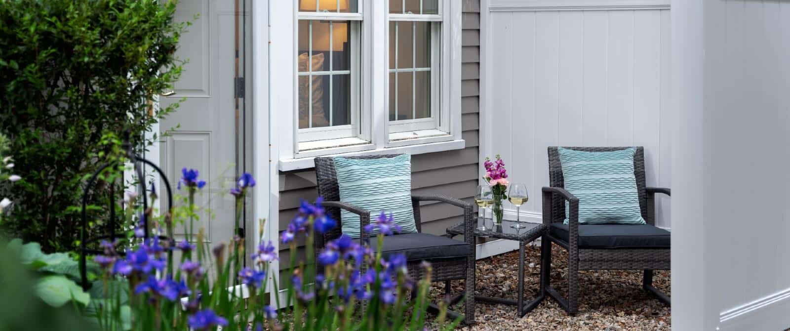 Private outdoor patio with two chairs and table holding wine glasses and vase of flowers