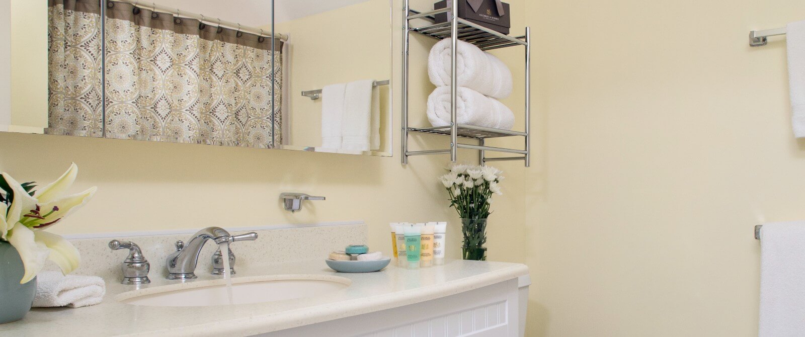 Bathroom with single sink, pale yellow walls, white hanging and rolled towels and large mirror