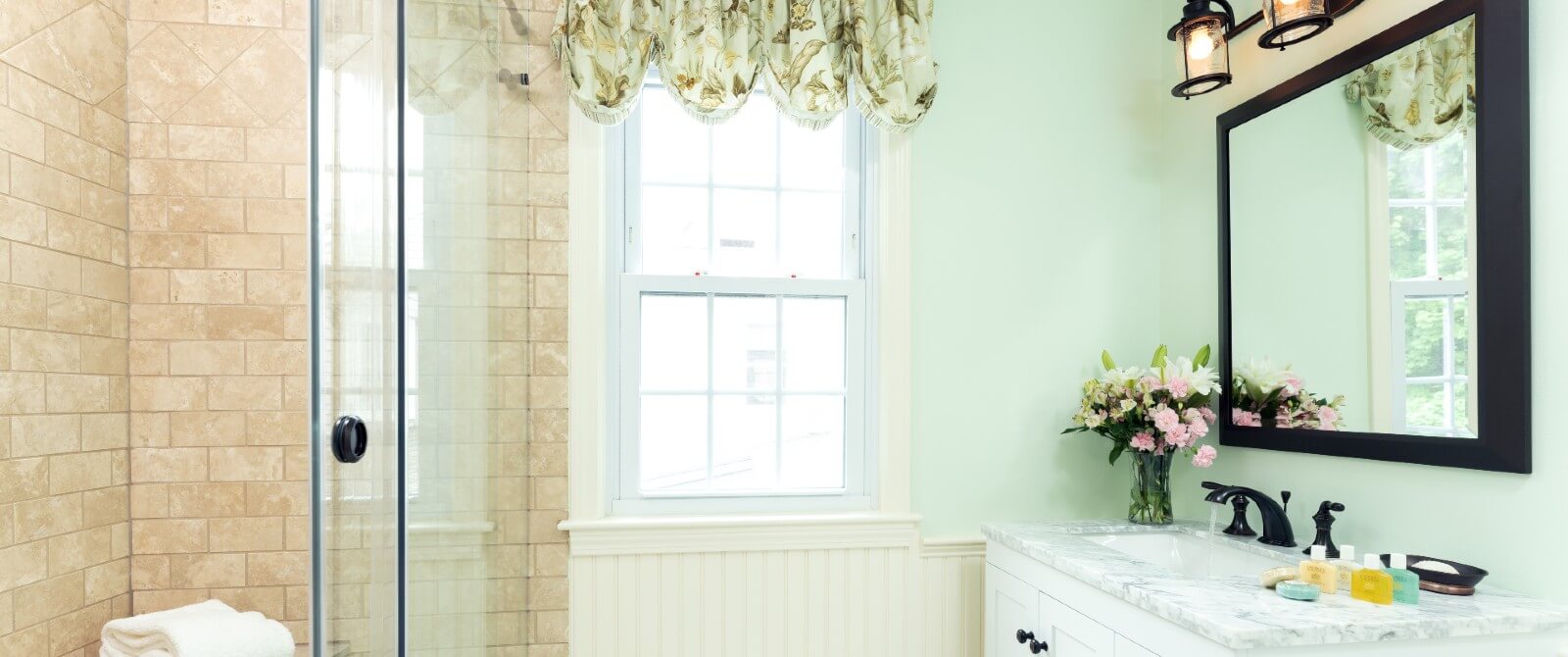 Bathroom with tiled shower, vanity under black framed mirror and bright window