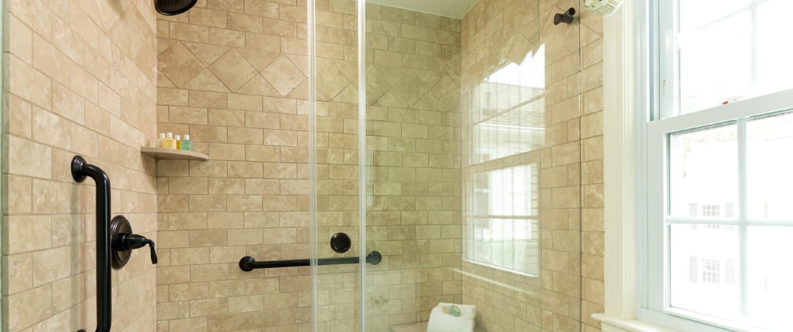 Large tiled shower with black accents in a bathroom with a bright window