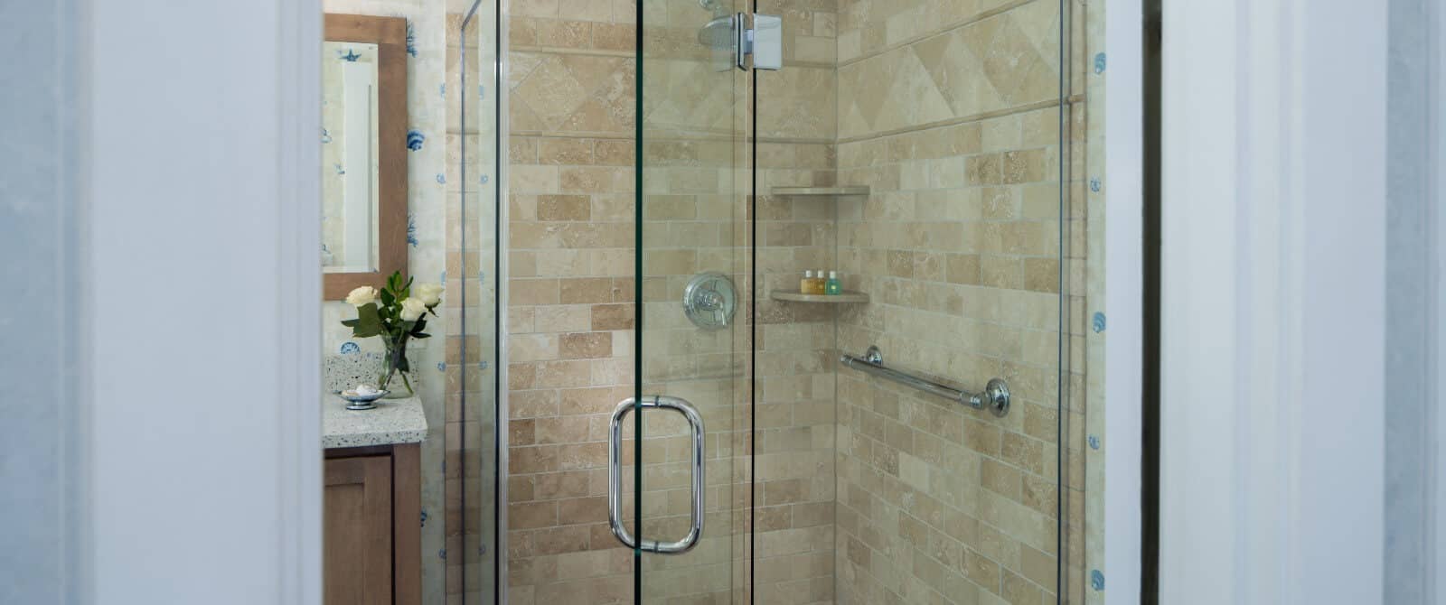 Bathroom with corner tiled shower and vanity with vase of white flowers