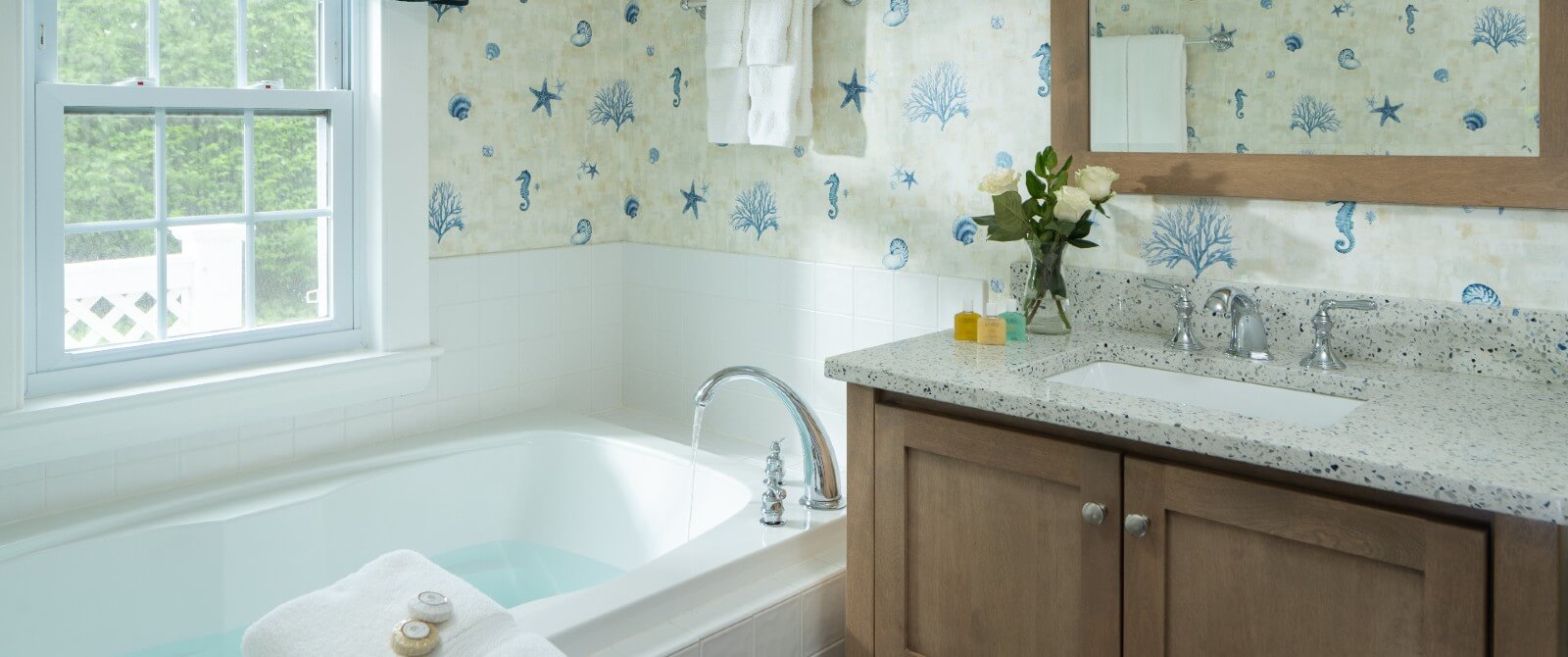 Bathroom with large soaker tub under a window, vanity and decorative wallpaper