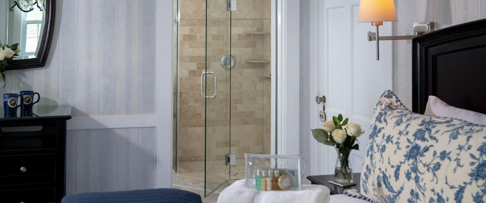 Bed with floral pillows, dresser with mirror and doorway into bathroom featuring tiled shower