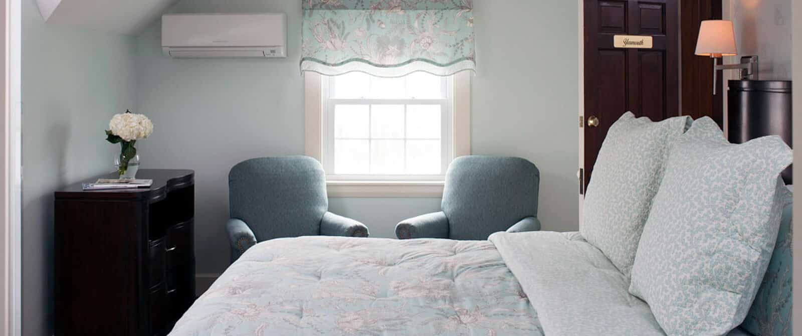 Bedroom with bed, dresser and two sitting chairs below a single bright window