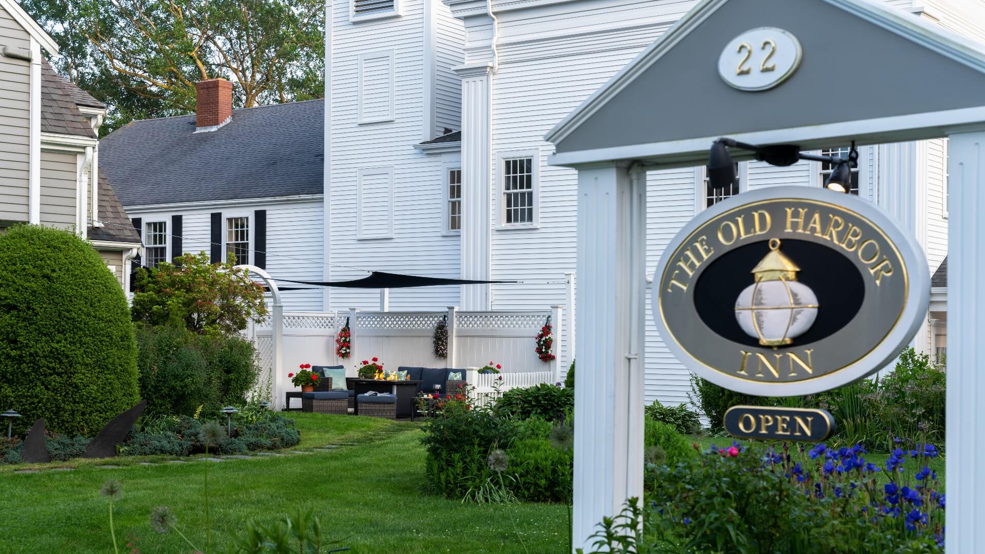 Grey, navy and gold oval business sign on white posts by a white home and outdoor fire pit area