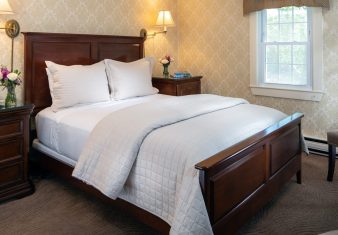 Elegant bedroom with bed in white quilt, decorative wallpaper and sitting chair by a window