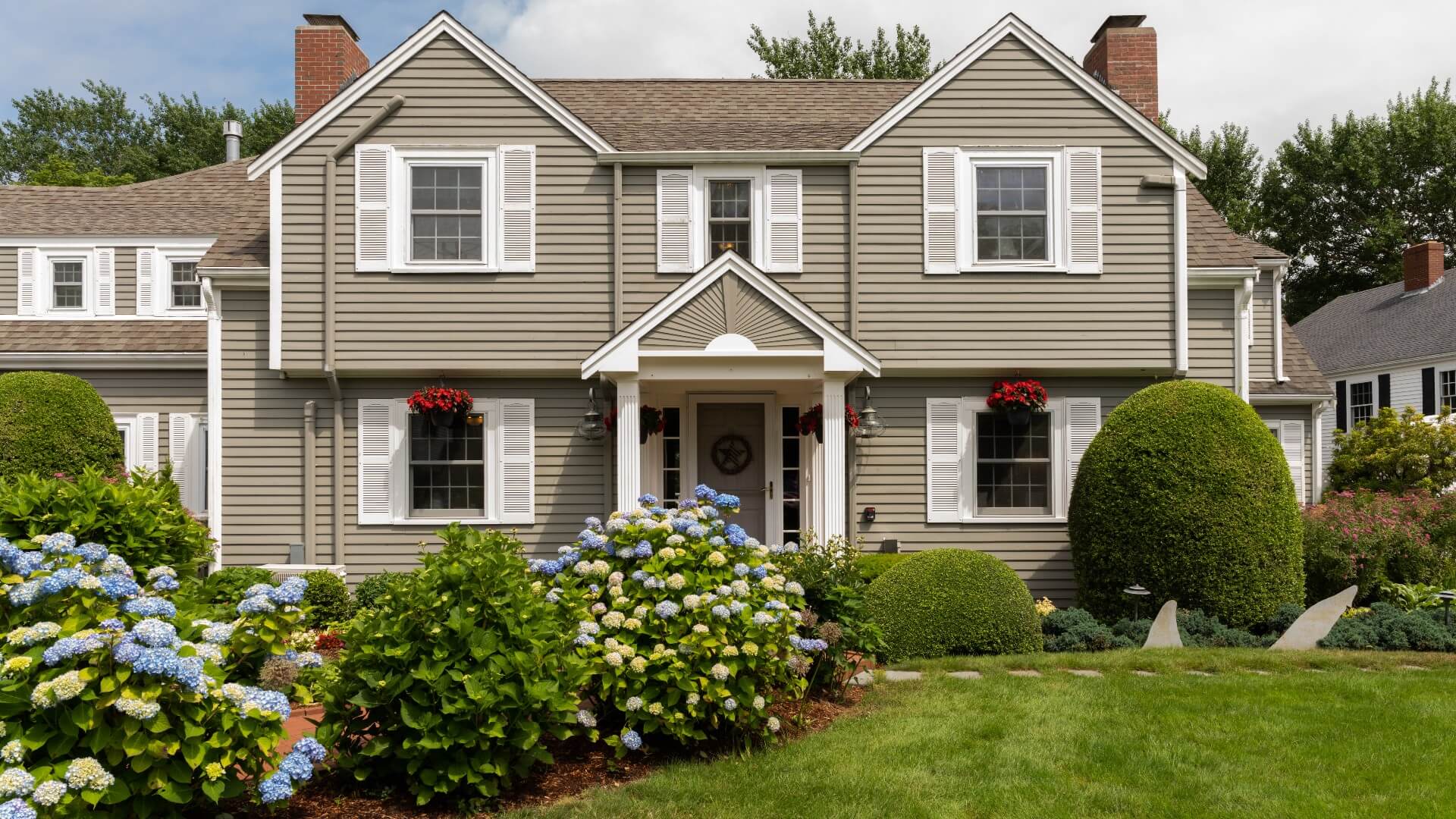 Front facade of a large home with brown siding, white shutters, and lush landscaping