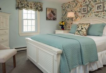 Elegant bedroom with floral wallpaper, queen bed, sitting chairs and window