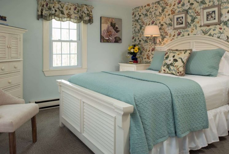 Elegant bedroom with floral wallpaper, queen bed, sitting chairs and window