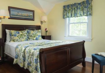 Bedroom with pale yellow walls, bed with floral quilt and bright window