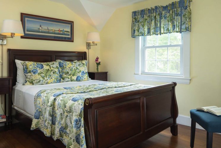 Bedroom with pale yellow walls, bed with floral quilt and bright window