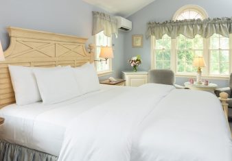 Spacious bedroom with king bed in white linens, and two sitting chairs under a bright window
