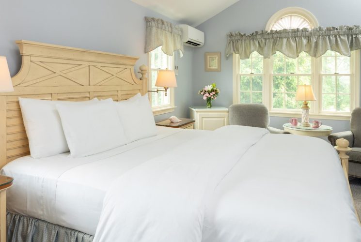 Spacious bedroom with king bed in white linens, and two sitting chairs under a bright window