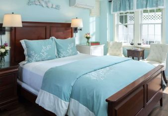 Bedroom with pale blue hues, white sitting chairs and door open to private patio