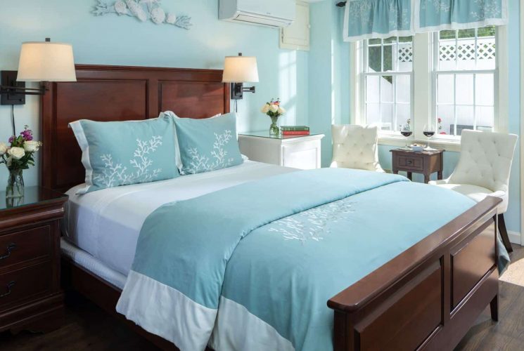 Bedroom with pale blue hues, white sitting chairs and door open to private patio