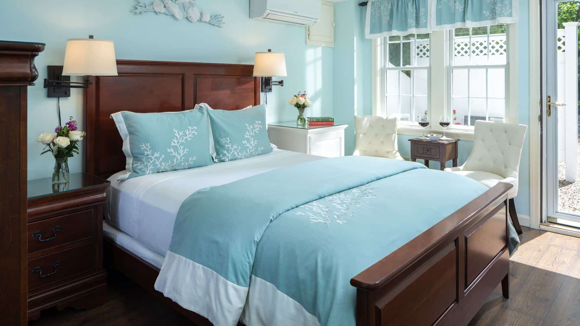 Bedroom with pale blue hues, white sitting chairs and door open to private patio