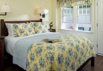 Bright bedroom with bed in floral quilt, large windows and door to private patio