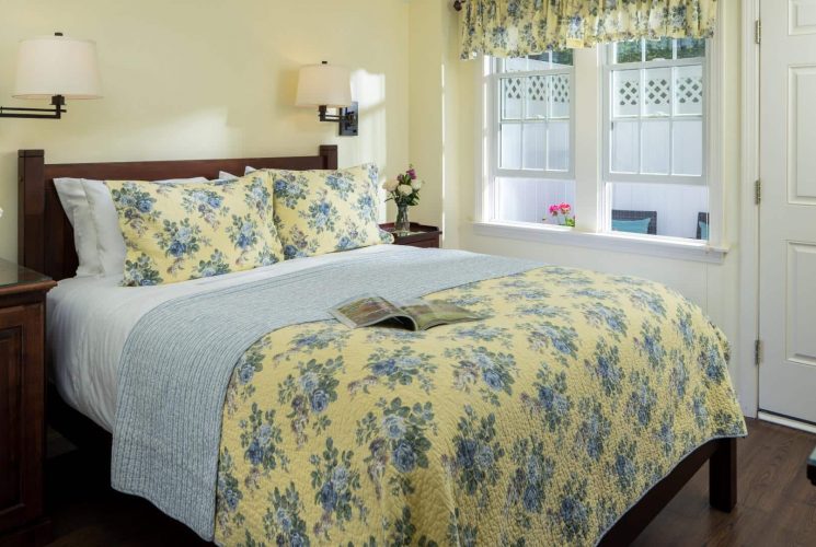 Bright bedroom with bed in floral quilt, large windows and door to private patio