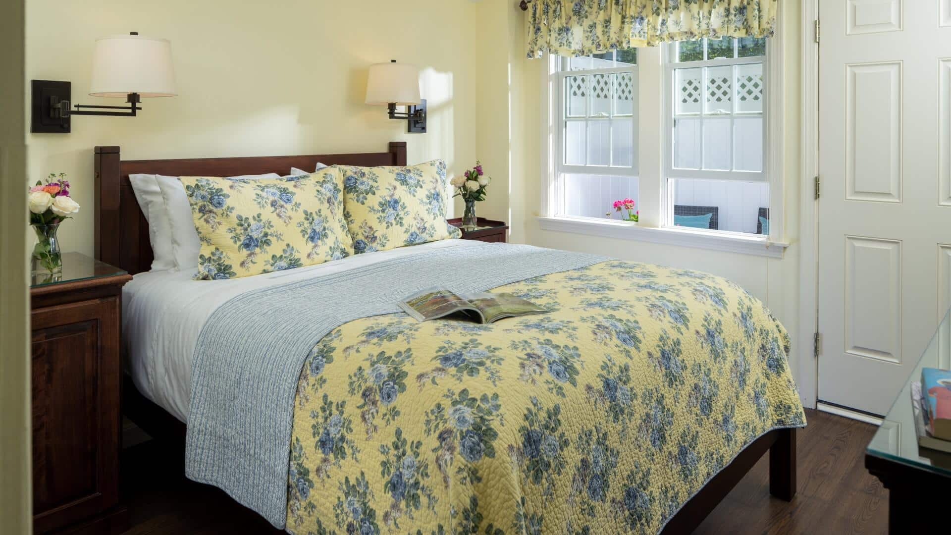 Bright bedroom with bed in floral quilt, large windows and door to private patio
