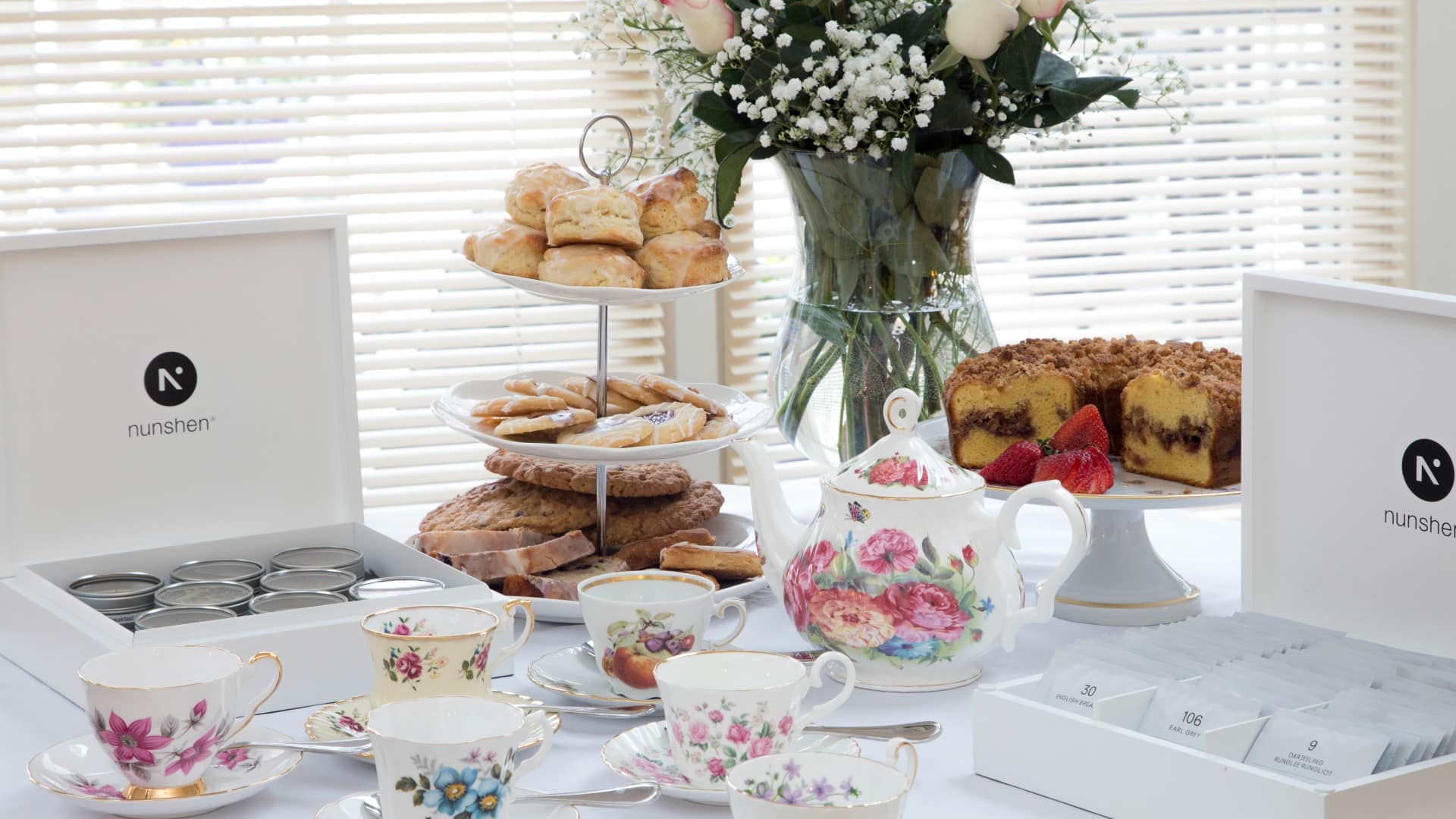 Table set for tea with floral cups and pitcher, vase of flowers and tower with baked goods