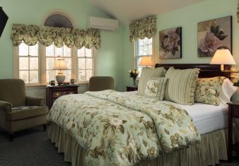 Elegant bedroom with king bed, two sitting chairs under a large window, and fireplace