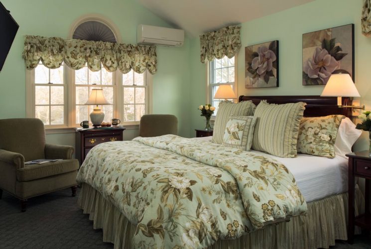 Elegant bedroom with king bed, two sitting chairs under a large window, and fireplace