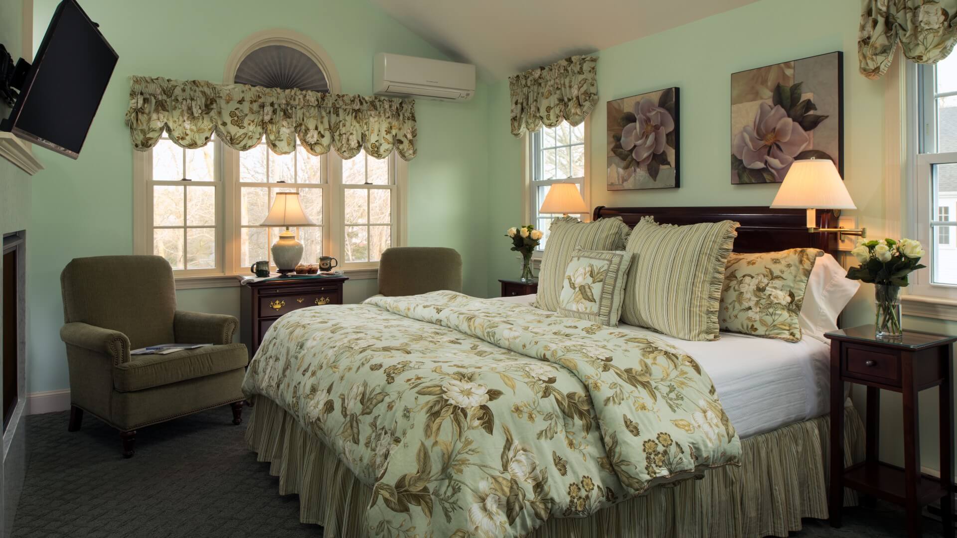 Elegant bedroom with king bed, two sitting chairs under a large window, and fireplace