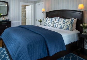 Elegant bedroom in blue hues with king bed, dresser with mirror and doorway into attached bathroom