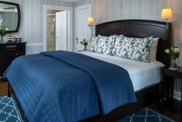 Elegant bedroom in blue hues with king bed, dresser with mirror and doorway into attached bathroom