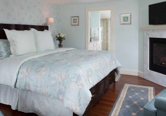 Guest room with mahogany bed, wood floors and TV hung over a gas fireplace