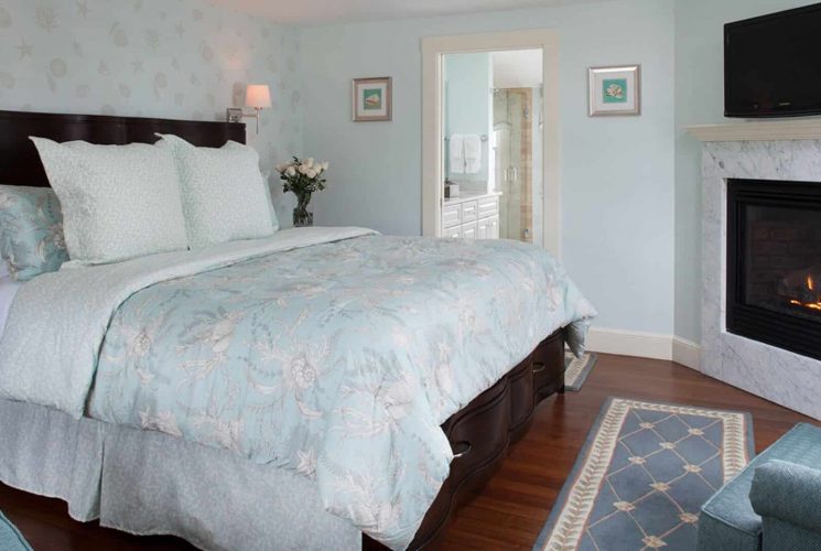 Guest room with mahogany bed, wood floors and TV hung over a gas fireplace