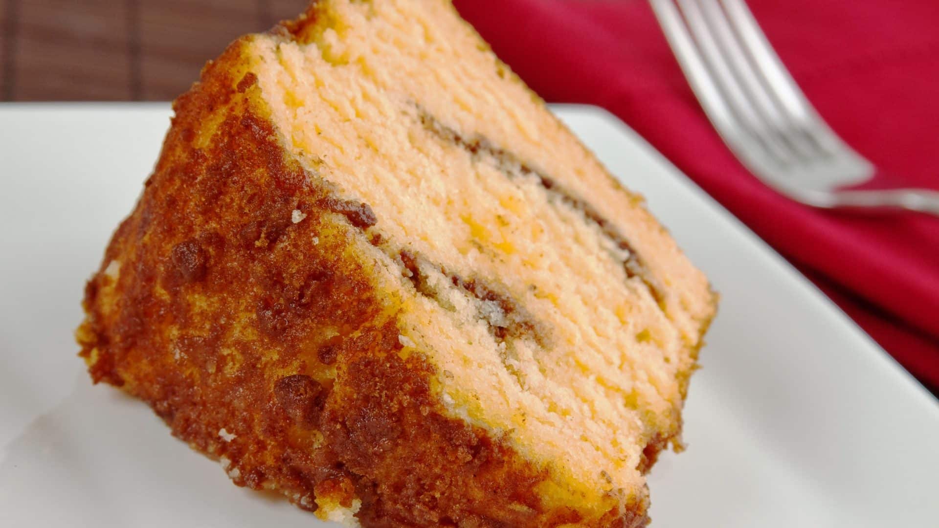 Slice of coffee cake on a white plate served with a fork and red napkin