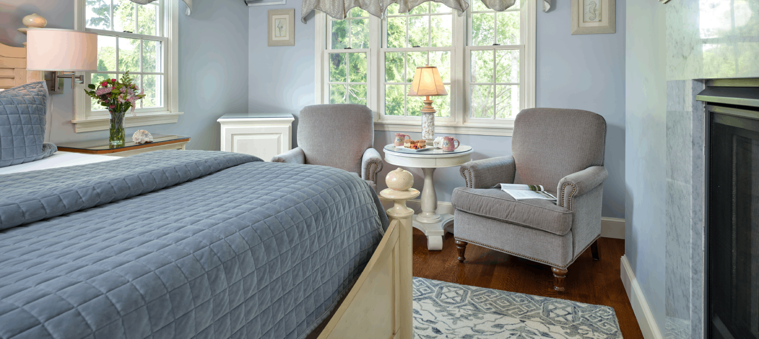 A view of a luxury room with king bed, two reading chairs, fireplace, smart TV and small fridge