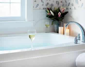 White bathtub topped with fresh flowers, three multi-height lit candles and two wine glasses filled with white wine